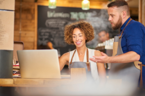 Co-owners review their daily tasks on a laptop on a store counter.